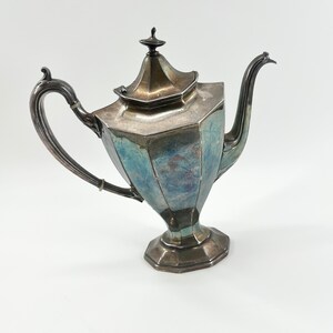 May include: A silver teapot with a octagonal body and a lid with a finial. The teapot has a spout and a handle.