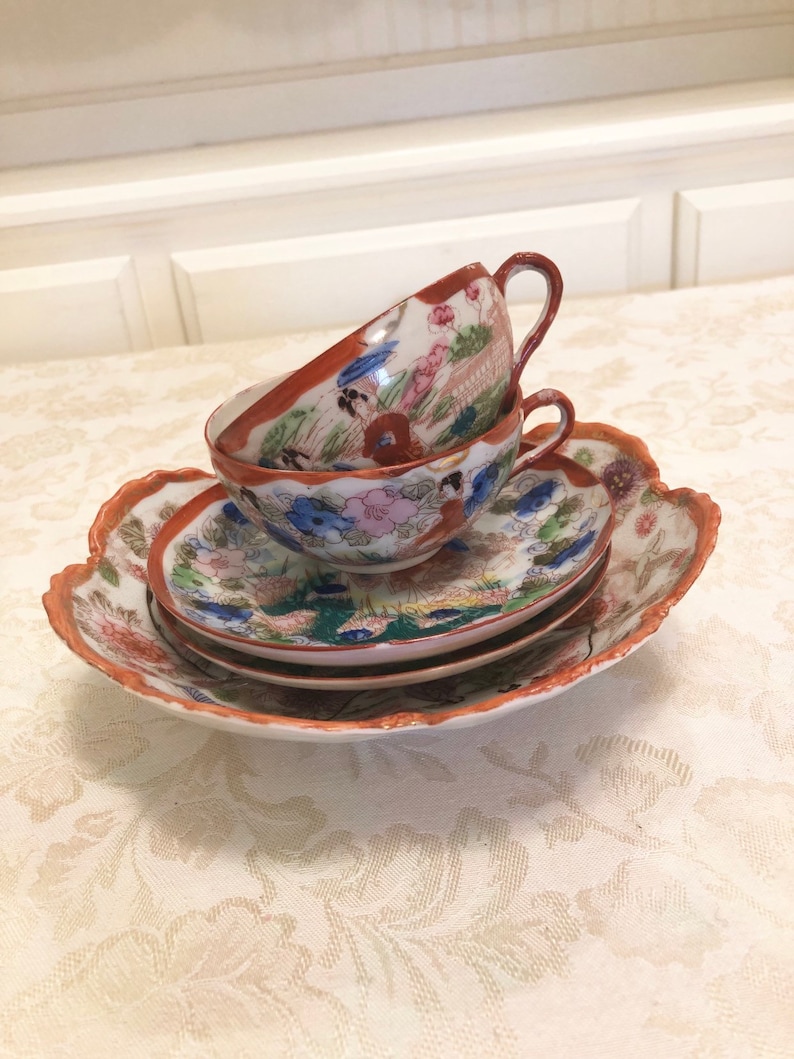 Antique Rose Medallion Chinese Lotus Nut Bowl And Tea Cups And Saucers Detailed In Gold And Red Trim Framing The Elegant Garden With Ladies