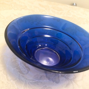 May include: A deep blue glass bowl with a rounded shape and a smooth, shiny surface. The bowl has a series of concentric rings on the inside, creating a layered effect.
