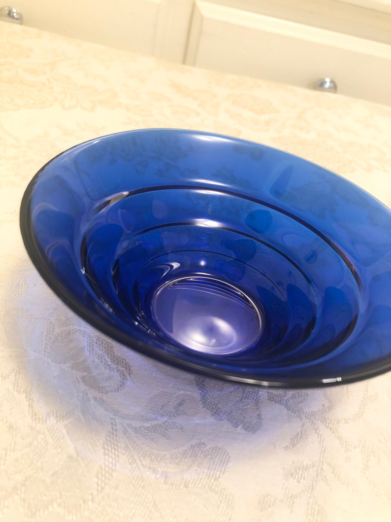 May include: A deep blue glass bowl with a rounded shape and a smooth, shiny surface. The bowl has a series of concentric rings on the inside, creating a layered effect.
