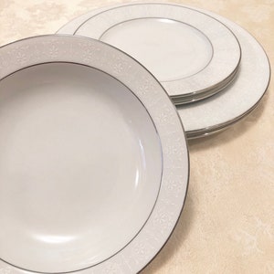 May include: Three white ceramic plates with a silver rim and a delicate floral pattern. The plates are stacked on top of each other.