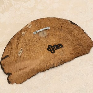 May include: The back of a wooden round sign with a metal hanger attached. The sign has a wood grain pattern and the words "PRS" are burned into the wood.
