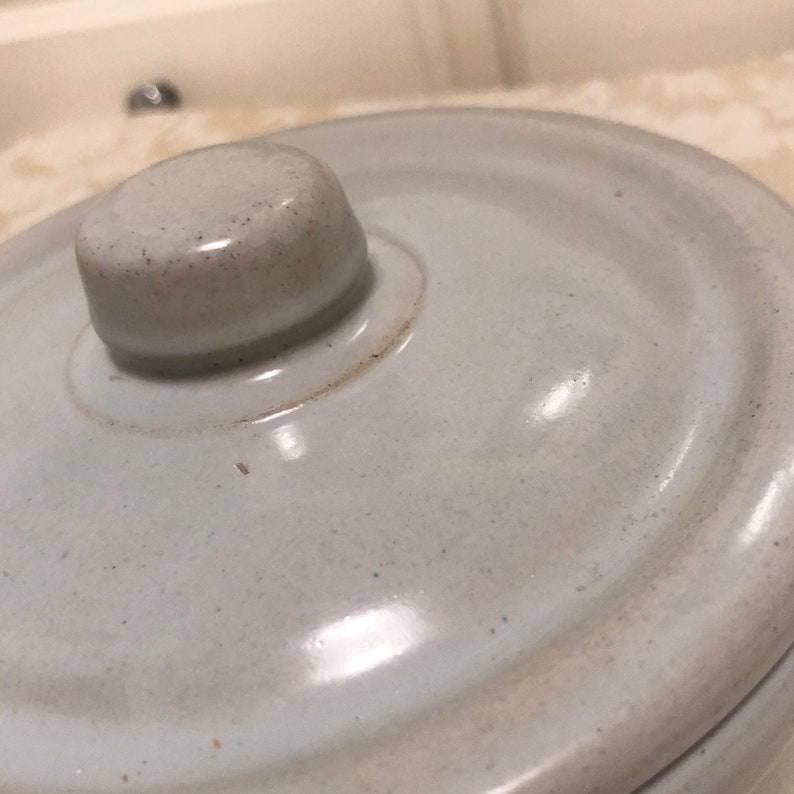 May include: A white ceramic lid with a round knob on top. The lid has a smooth, glossy finish and a slightly textured surface.