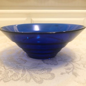 May include: A cobalt blue glass bowl with a fluted design. The bowl is empty and sitting on a white tablecloth.