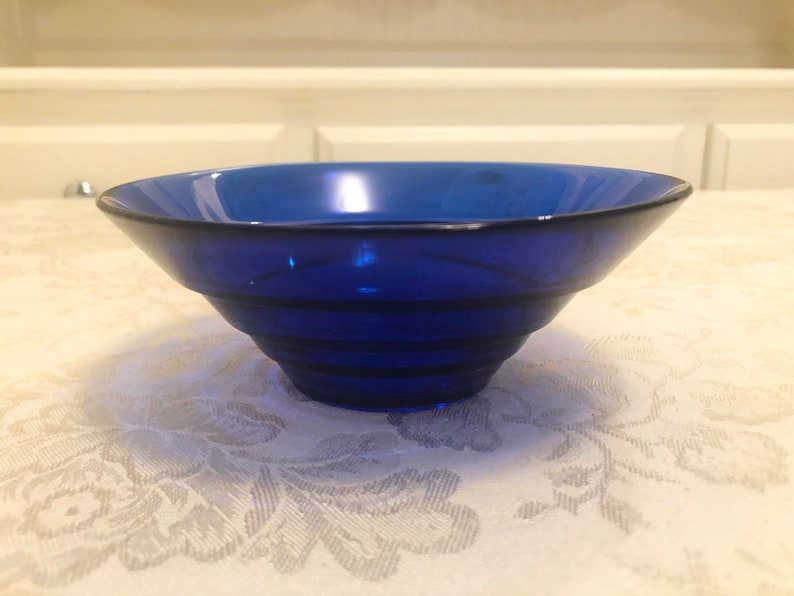 May include: A cobalt blue glass bowl with a fluted design. The bowl is empty and sitting on a white tablecloth.