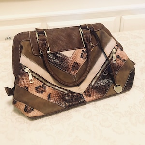 May include: A brown, beige, and black leather handbag with a snakeskin pattern. The bag has a top zipper closure and a gold-tone zipper pull.