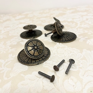 May include: Five antique brass cabinet knobs with a decorative floral design and matching screws. The knobs have a raised center with a starburst pattern.