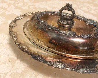 May include: Silver plated oval serving dish with a lid. The lid has a decorative handle with grape clusters. The dish has a scalloped edge with grapevine designs.
