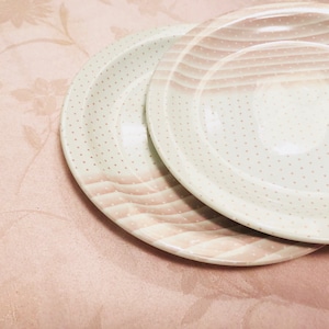 May include: Two white ceramic plates with a pink and white polka dot pattern. The plates are stacked on top of each other.