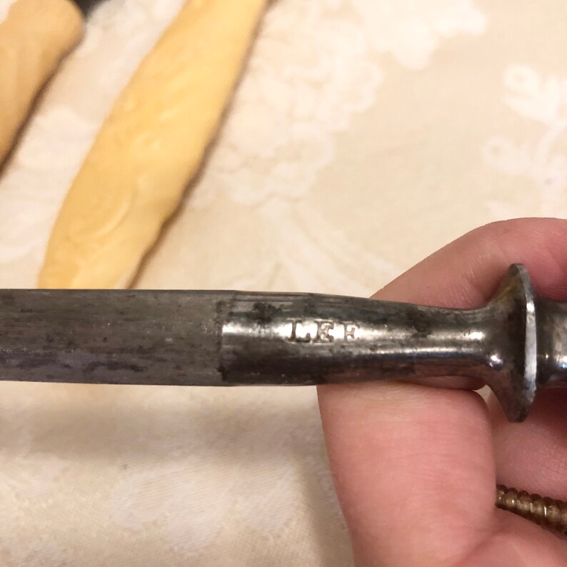 May include: A close-up of a metal sharpening steel with the inscription "L.E.R." on the side.