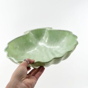 May include: A light green, shell-shaped serving bowl made of plastic. The bowl has a smooth, glossy finish and a slightly rippled edge.