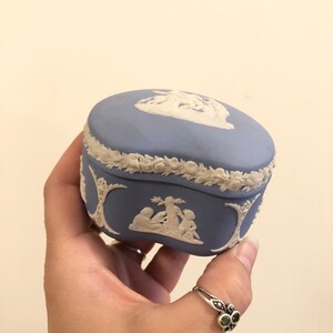 May include: A blue and white ceramic trinket box with a raised design of figures and a floral border.
