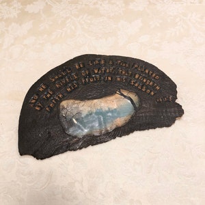 May include: A wooden plaque with a rustic brown finish and a painted scene of a lake with trees. The plaque has a quote from the Bible, "And he shall be like a tree planted by the rivers of water, that bringeth forth his fruit in his season."
