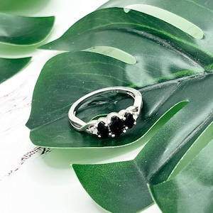 May include: A silver ring with a twisted band and three black oval-shaped gemstones.