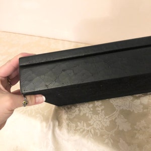 May include: A black rectangular box with a textured surface. The box is made of wood and has a lid.