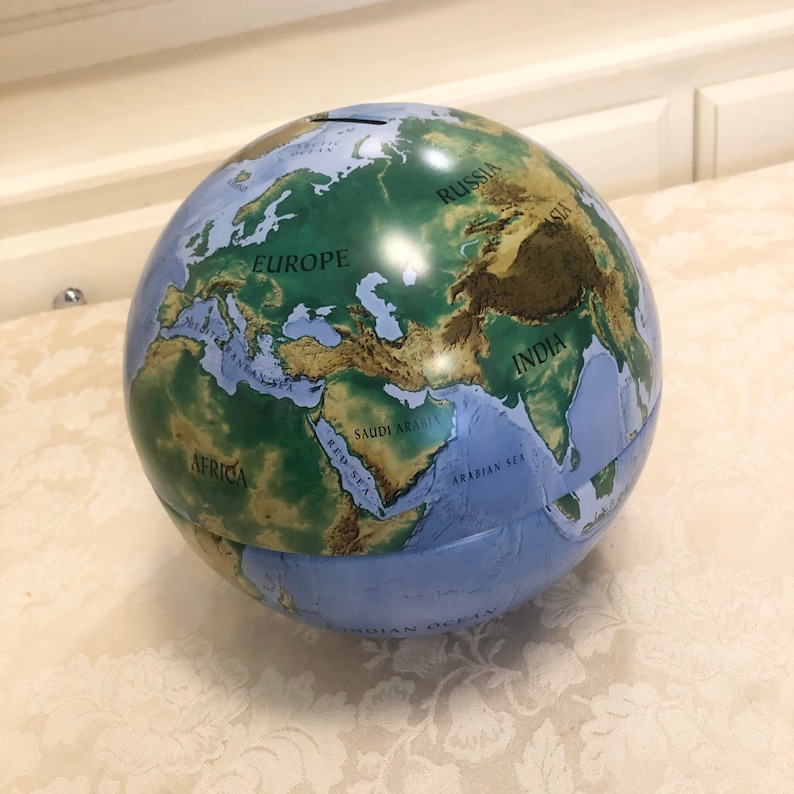 May include: A blue and green globe with a map of the world. The globe has a slot on the top for coins, making it a piggy bank. The globe shows the continents of Africa, Europe, Asia, and Australia. The globe also shows the oceans, including the Indian Ocean, the Atlantic Ocean, and the Pacific Ocean.