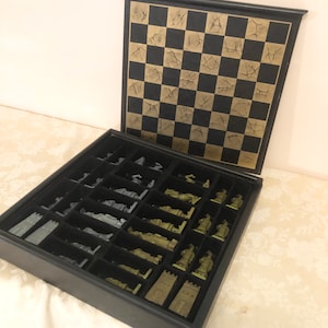 May include: A black leather chess set with a gold-colored board and silver and green chess pieces. The pieces are stored in a compartment below the board.