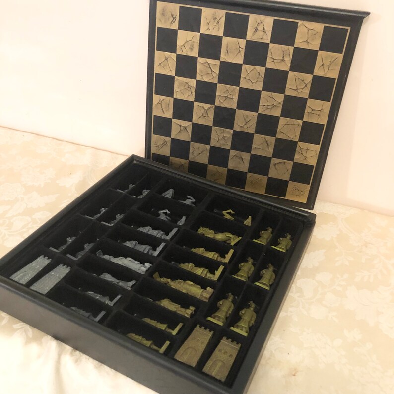 May include: A black leather chess set with a gold-colored board and silver and green chess pieces. The pieces are stored in a compartment below the board.