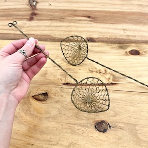 May include: Two antique wire mesh kitchen tools with long handles. The mesh is a fine, open pattern, and the handles are twisted wire. One handle has a decorative loop at the end. The tools are a muted brass color.