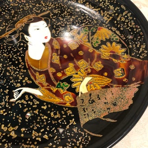 May include: A black lacquer plate with a gold and silver design of a woman in a kimono. The woman is surrounded by gold and silver dots and flowers.