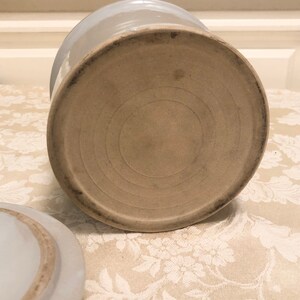 May include: The bottom of a white ceramic crock with a circular, concentric ring design.