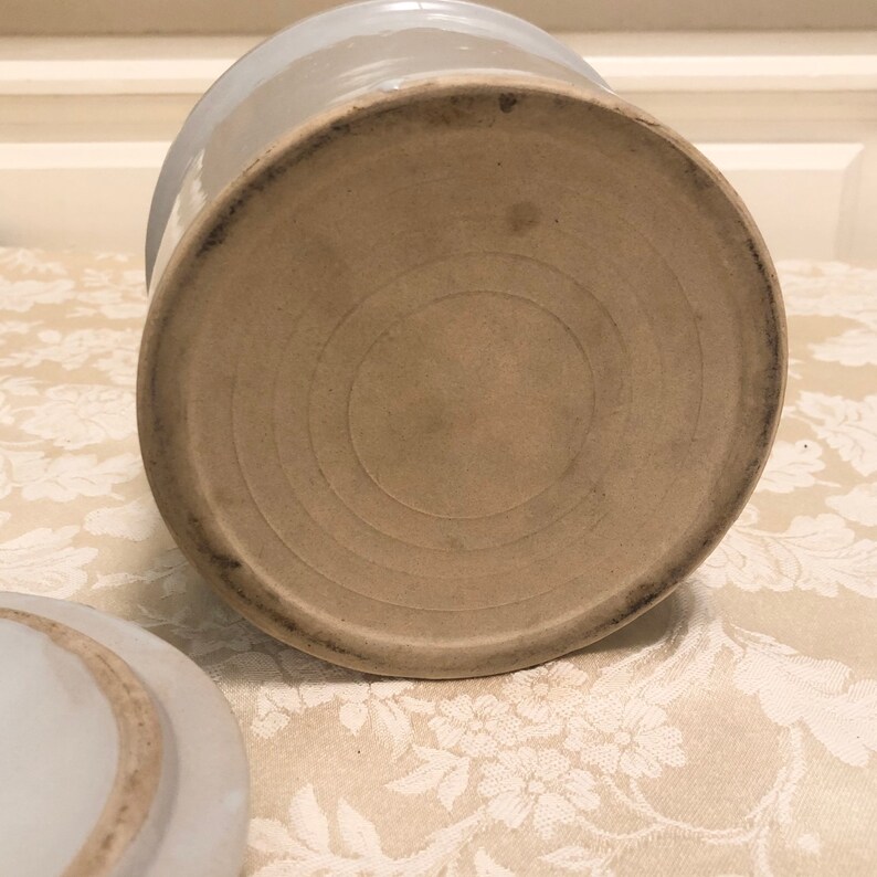 May include: The bottom of a white ceramic crock with a circular, concentric ring design.