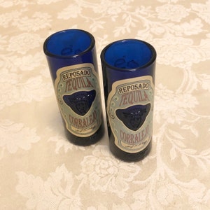 May include: Two blue shot glasses with a white label that reads "Reposado Tequila Corralejo".