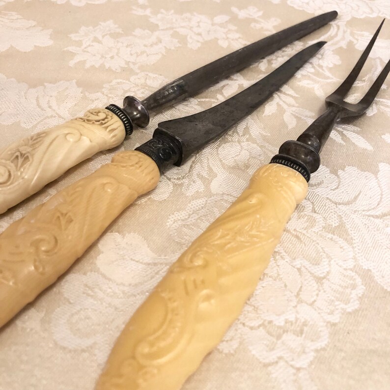 May include: Three antique carving knives with ivory handles. The handles have an intricate floral design. The blades are made of metal and have a dull finish.