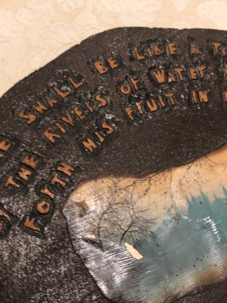 May include: A brown, textured, rectangular sign with the text "I SHALL BE LIKE THE RIVERS OF WATER FOYTH MISS FRUIT IN T" printed in gold lettering. The sign has a faded image of a forest scene in the background.