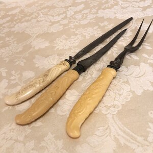 May include: Three antique carving knives with ornate ivory handles. The blades are made of metal and have a dull finish.