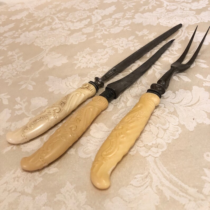 May include: Three antique carving knives with ornate ivory handles. The blades are made of metal and have a dull finish.