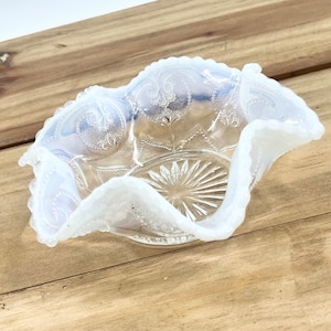 May include: A white milk glass bowl with a scalloped edge and a delicate floral pattern. The bowl is made of clear glass with a frosted finish.