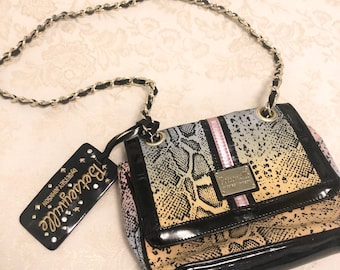 May include: A small black and multi-colored snakeskin patterned handbag with a gold chain strap and a black tag that says "Betsey Johnson" with rhinestones.