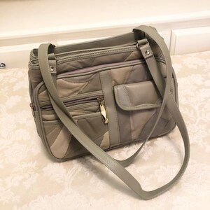 May include: A gray leather patchwork handbag with a long shoulder strap. The bag has multiple pockets and zippers.