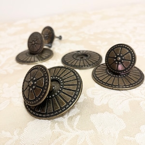 May include: Five antique brass cabinet knobs with a decorative sunburst design. The knobs have a raised center with a floral pattern.