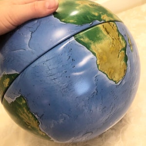 May include: A blue and green globe with a raised relief map of the Earth. The globe is made of plastic and has a shiny finish.