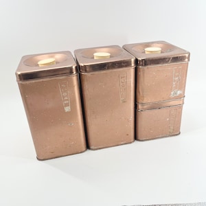May include: Four vintage brown metal canisters with white lids. The canisters are labeled "Sugar", "Tea", "Coffee", and "Flour".
