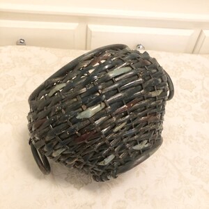 May include: A woven wicker basket with a dark brown and blue color scheme. The basket has two metal handles and a rounded shape.