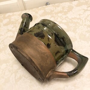May include: A green and brown ceramic watering can with a spout and handle. The can has a mottled glaze with brown and green accents.
