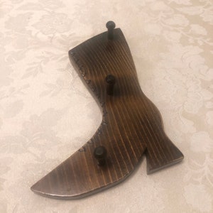 May include: Wooden boot-shaped key holder with three metal hooks. The boot is dark brown with a stitched design.