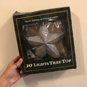 May include: A silver glitter star Christmas tree topper with 10 lights. The box says "Steady Burning or Single Flashing" and "10 Lights Tree Top".