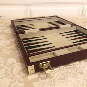 May include: A burgundy leather backgammon game set with a gold latch. The game board is open and shows the black and white playing pieces.