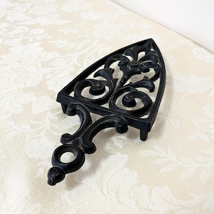May include: Black cast iron trivet shaped like an iron with an ornate design.