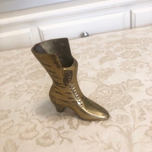 May include: A gold-colored metal boot shaped vase. The boot has a high heel and a lace-up design.