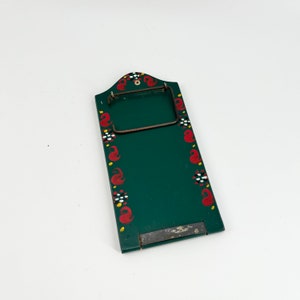 May include: A green wooden memo board with a metal clip and a painted design of red, white, and yellow flowers. The board has a black metal bottom.