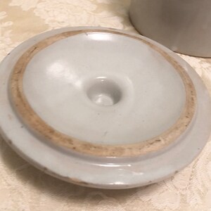 May include: White ceramic lid with a brown rim and a small hole in the center.