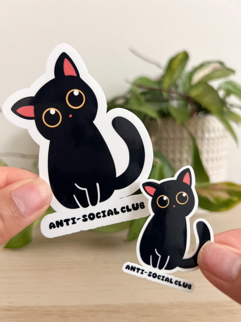 Puede incluir: Dos pegatinas de gato negro con el texto "ANTI-SOCIAL CLUB". Los gatos tienen ojos grandes y redondos, orejas internas rosas y contornos blancos. Una pegatina es m&aacute;s grande que la otra.