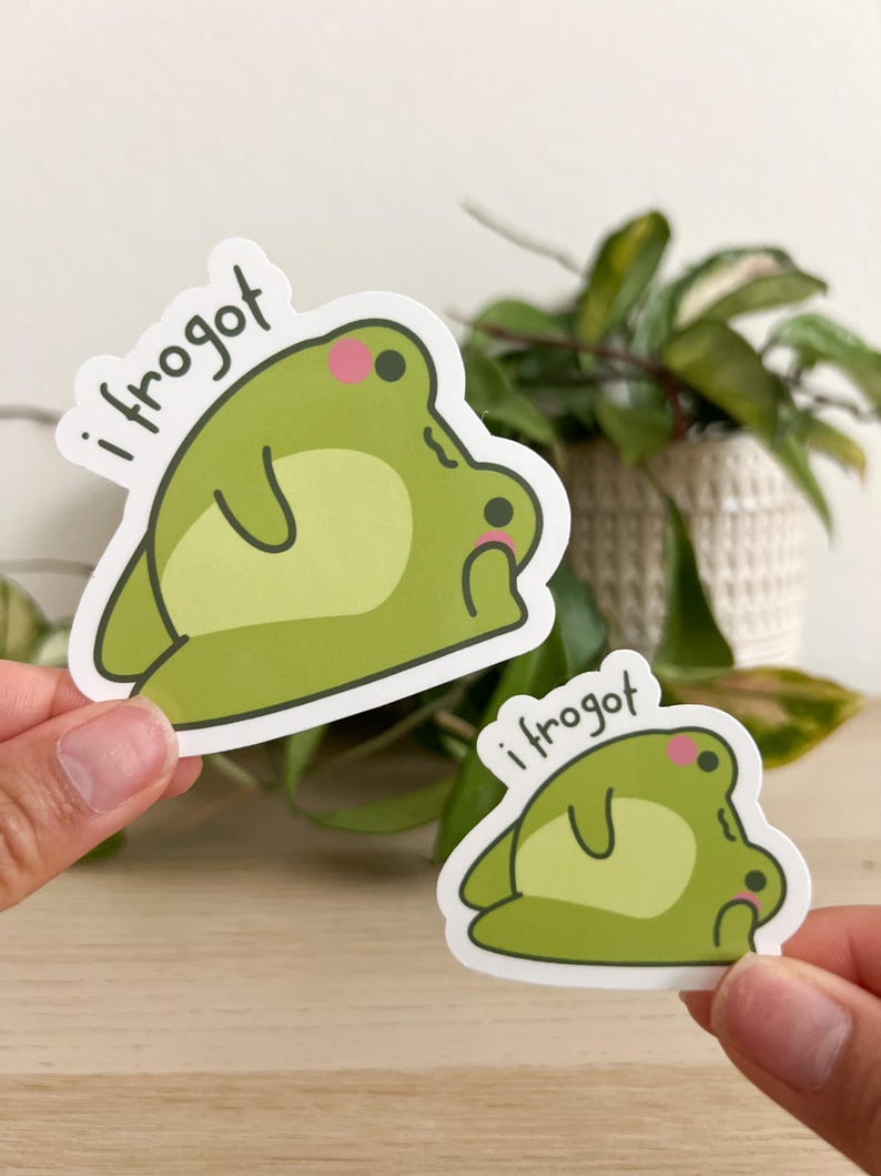 Op de afbeelding: Twee groene kikkerstickers met de tekst "i frogot". De kikkerstickers hebben een lichtgroen lichaam, een donkerdere groene buik en roze wangen. De ene sticker is groter dan de andere.