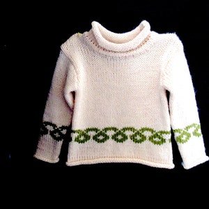 Pu&ograve; includere: Un maglione di lana bianco con un bordo verde intorno al collo e ai polsini. Il maglione ha un collo alto.