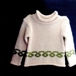 Pu&ograve; includere: Un maglione di lana bianco con un bordo verde intorno al collo e all'orlo inferiore. Il maglione ha un collo alto.